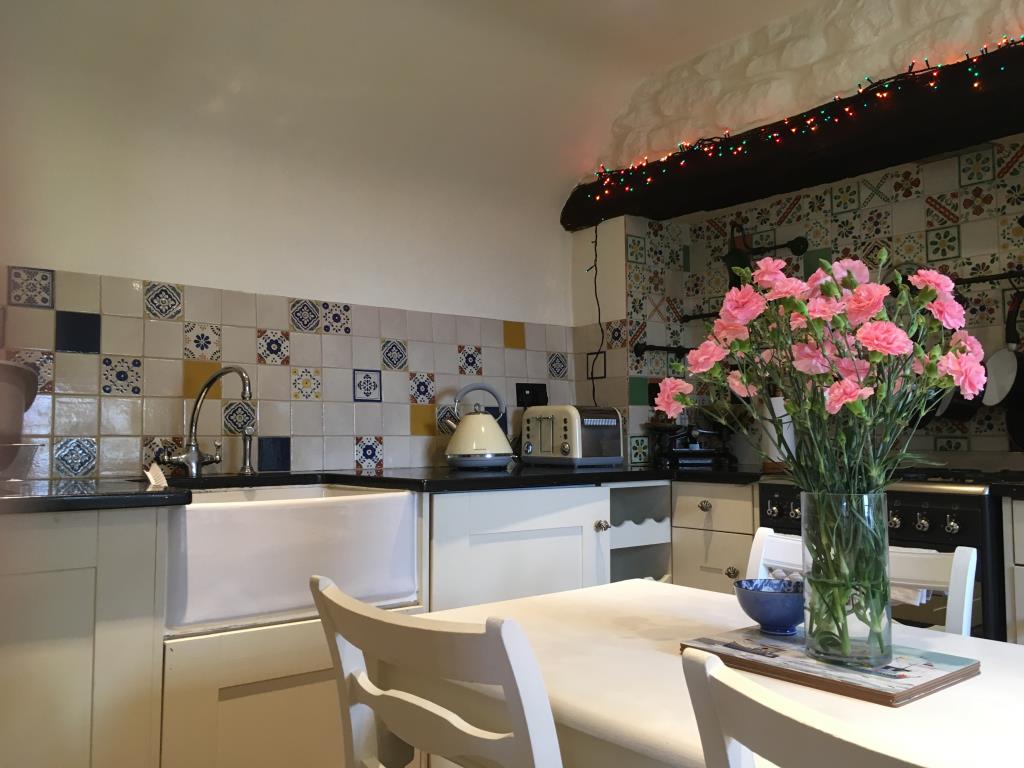 Lot: 138 - TWO-BEDROOM THATCHED COTTAGE FOR OCCUPATION OR INVESTMENT - Kitchen with wall tiles sink and table in foreground
